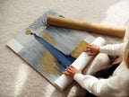 A woman is carefully rolling a fine art poster paper. She is ensuring its quality and preservation. The poster likely features abstract figure artwork with grey blue and gold colors. This demonstrates the care taken in preparing minimalist art for display.