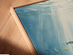 A close-up angled view of a canvas print in a floating frame. The underwater artwork depicts an ocean scene. This sea life wall art adds a coastal touch. The aqua blue painting enhances any room.