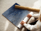 A woman carefully rolls fine art poster paper. She prepares a celestial artwork print. The fine art poster ensures a high-quality finish for your starry universe art. Perfect for any space.
