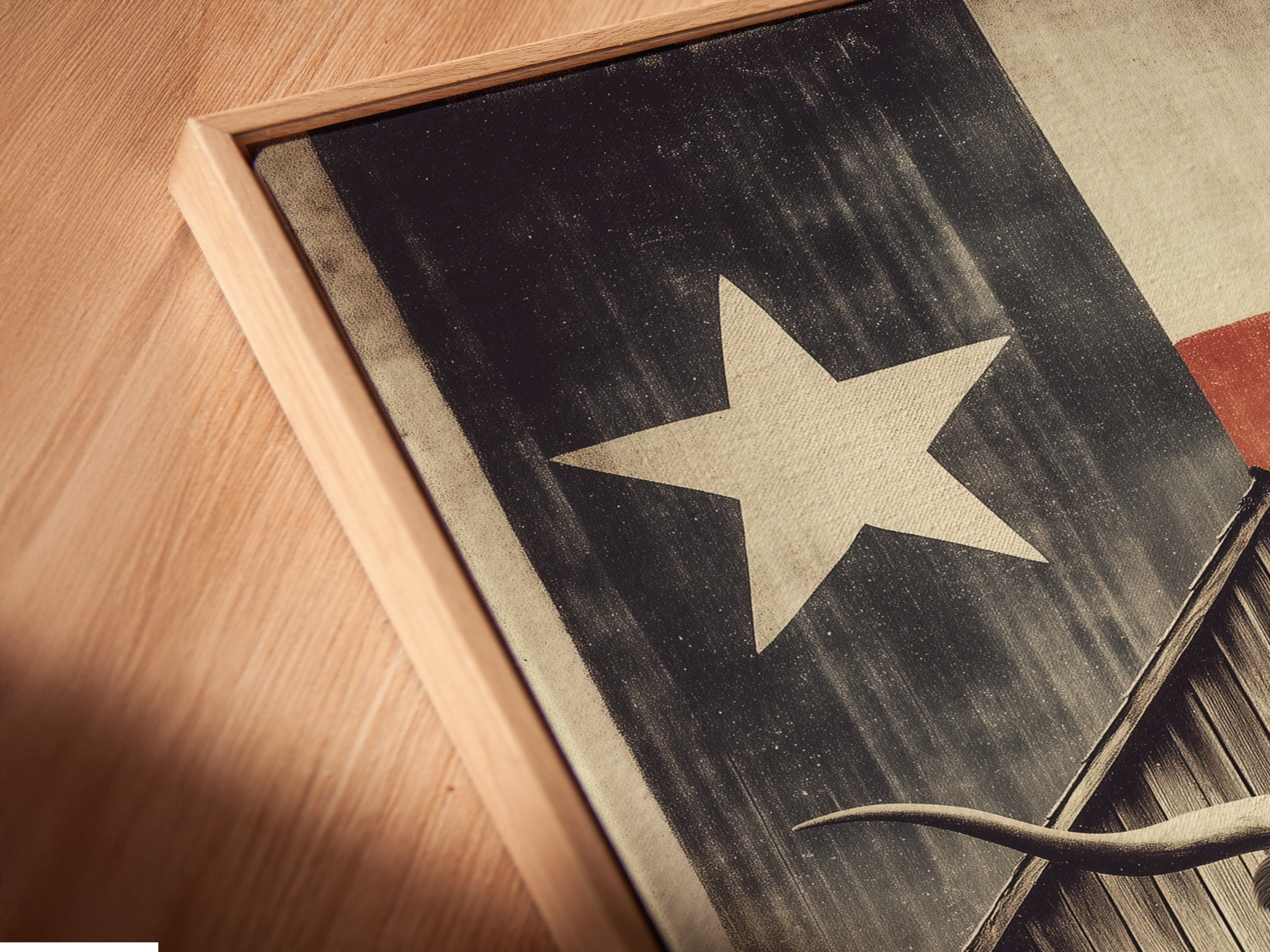 Close-up angled view of a Texas Longhorn canvas print. The artwork is displayed in a floating frame. The artwork features a longhorn in front of a wooden barn. A Texas flag is behind the barn. This adds depth and style to this rustic art.