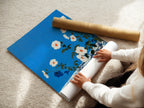 A woman is carefully rolling a fine art poster paper. The floral artwork poster features azure blue tones. The botanical print is perfect for creating modern wall decor. This fine art paper ensures quality.