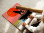 A woman carefully rolls a fine art poster paper of the Wolf Moon artwork. This abstract wildlife print features a howling wolf under a colorful sunset. The poster paper ensures a high-quality reproduction. Add a vibrant touch to your bedroom decor with this fine art print. Perfect for art lovers.