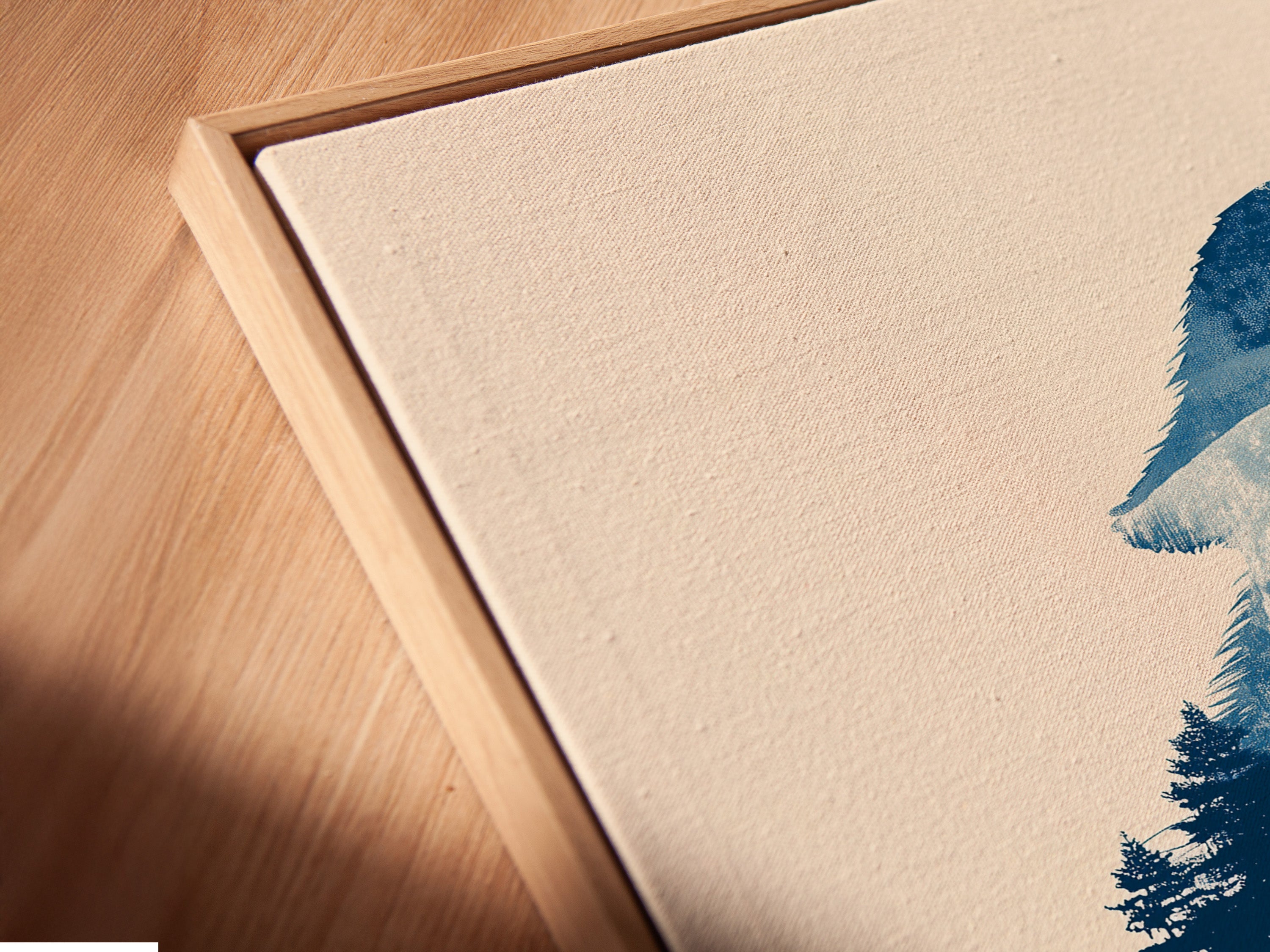 Angled close up of a canvas print in floating frame. The artwork features a wolf silhouette in a forest with a moon. The artwork is reflected in the water below. Great as navy blue nature decor.