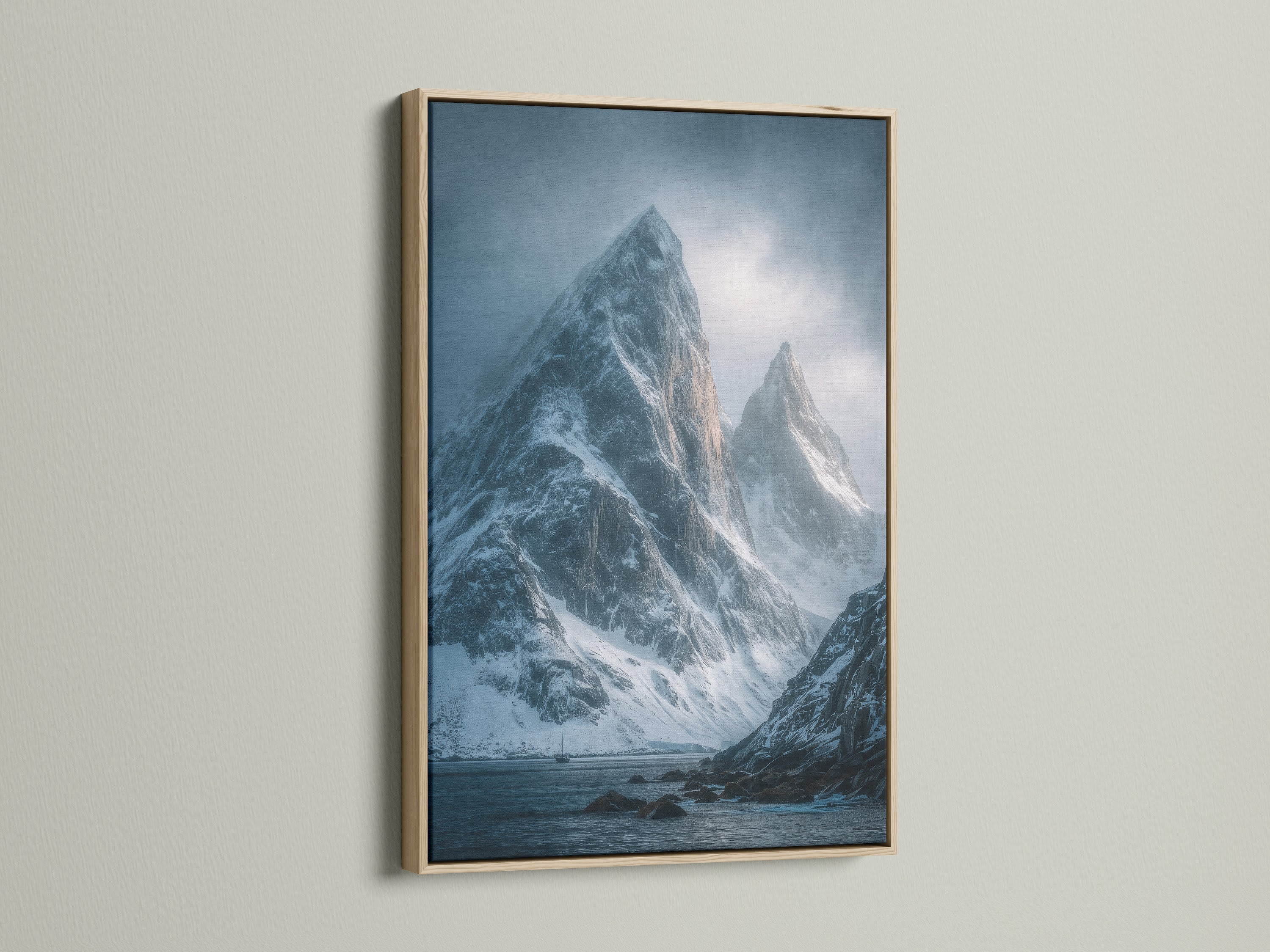 An oak frame showcases a captivating mountain canvas print. The coastal art depicts snow capped peaks in a moody landscape. It's perfect nature wall art for Scandinavian or coastal styles.