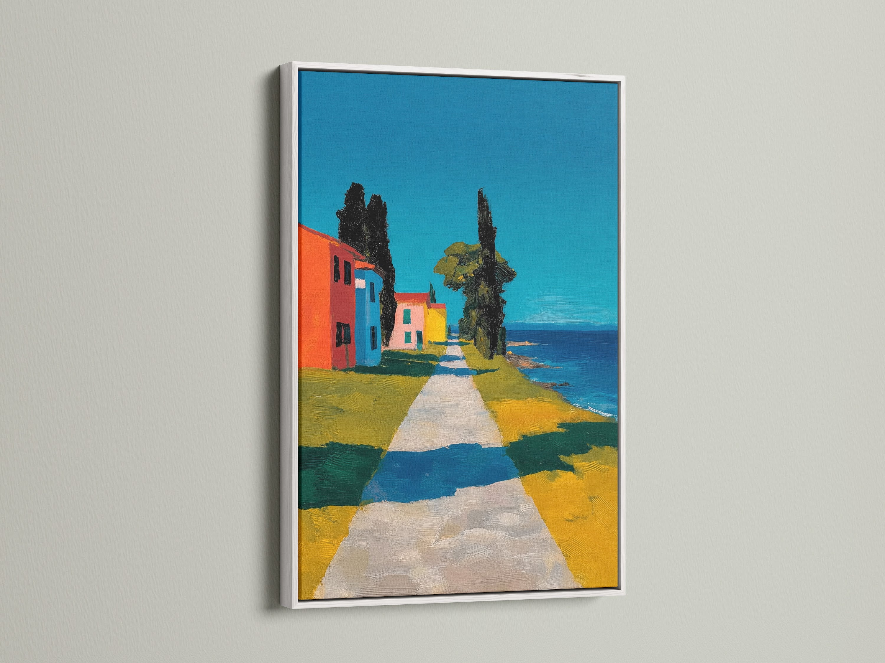 Artwork with a white frame is presented. The art features a path leading to colorful buildings. It is a coastal scene under a bright sky. The white frame offers a clean modern look. It makes the artwork stand out.