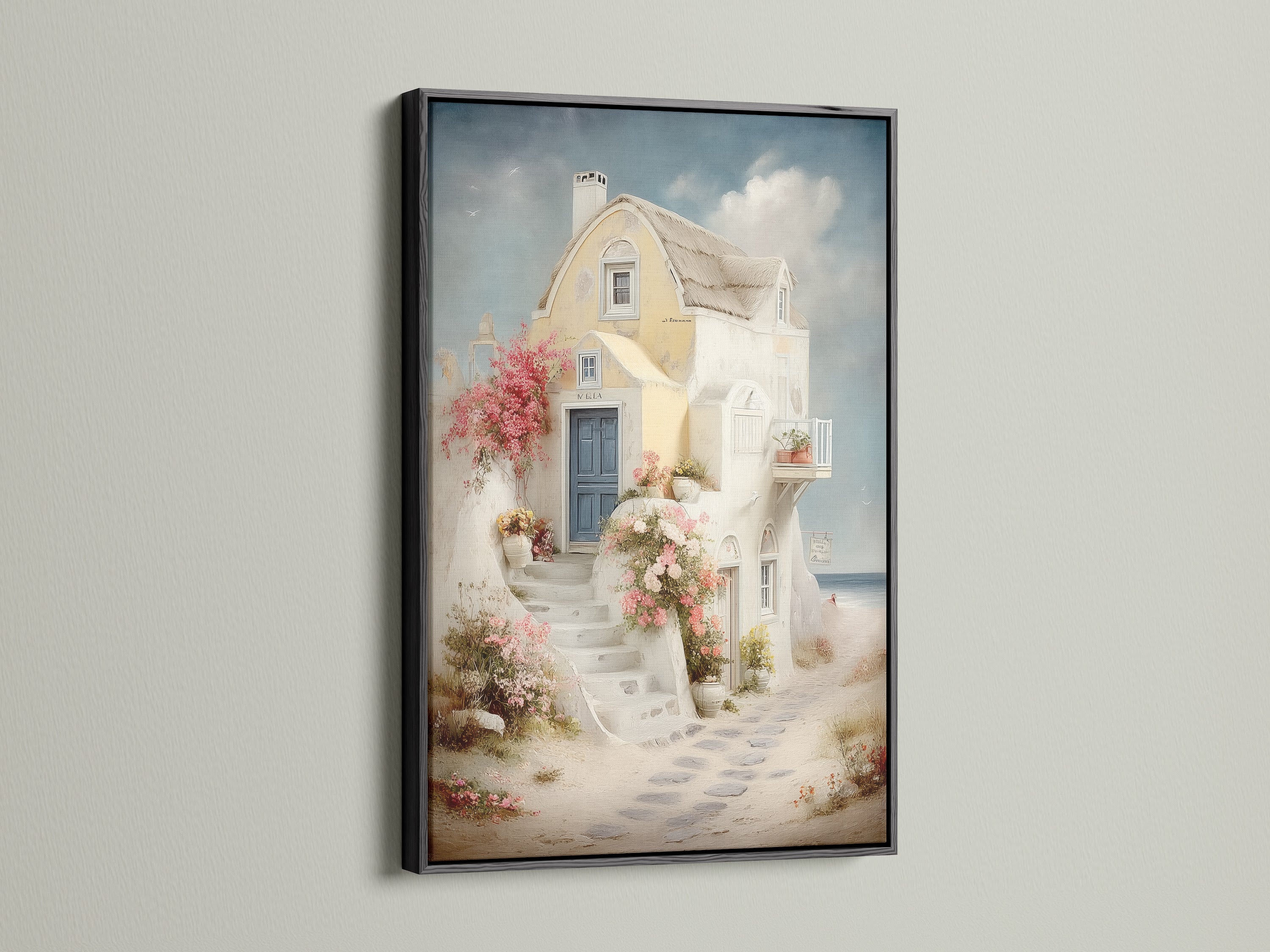 Coastal artwork in a black frame. The artwork features a Mediterranean house canvas with a blue door and floral stairway. Perfect for adding Greek island art to your vacation home decor. This sea view print enhances any space. Ideal for living room wall art.