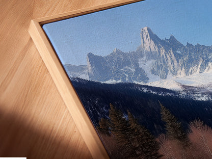 A close-up angled view reveals a canvas print in a floating frame. The artwork showcases a mountain chalet scene. Its snowy Alps landscape provides rustic charm. The floating frame adds a modern touch. Perfect lodge artwork for cabin decor.