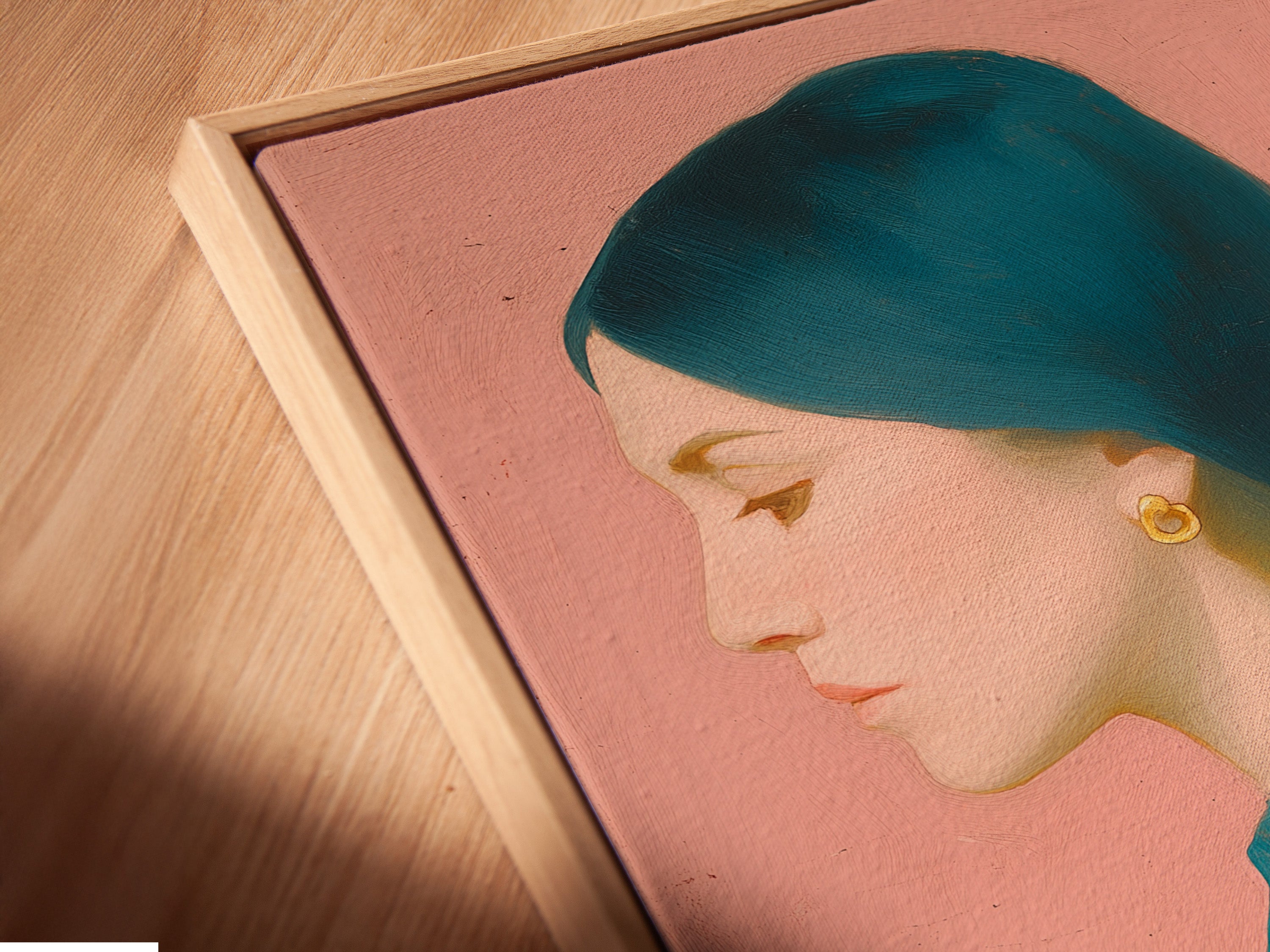 Close-up angled view of a canvas print in a floating frame. The artwork has a woman with teal hair and shirt. The background is pink and she has a shadow. This framing style gives the art a sophisticated gallery look.