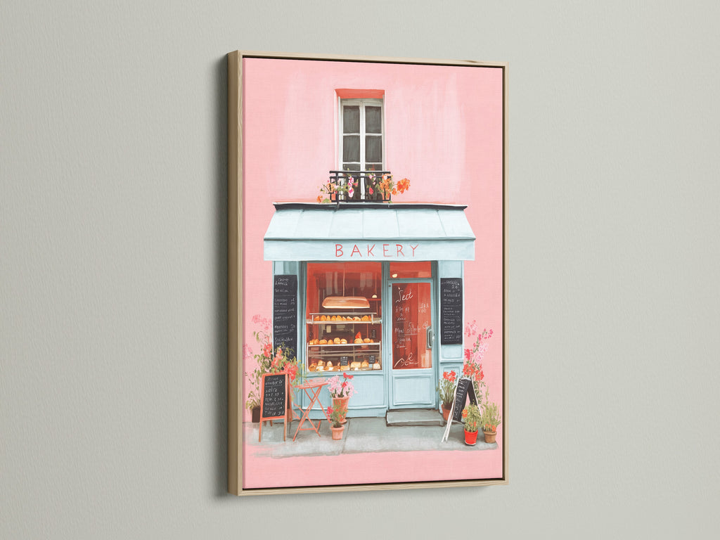 Artwork displayed in an oak frame. The art depicts a quaint bakery with a pink facade and inviting blue accents. The oak frame enhances the artwork's charm. A perfect addition to bring warmth and character to your living space with this piece.