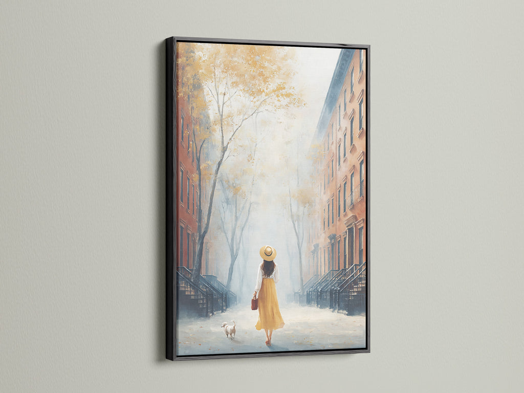 City Street artwork in a black frame. The artwork features a woman and her dog on a townhouse-lined street. The black frame adds a modern touch. This piece would be a great addition to office wall art. The artwork has fall colors.