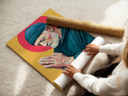 A woman carefully rolls a fine art poster paper print of the Praying Man artwork. This shows the care in handling and preserving the spiritual canvas. The teal and gold artwork is ready to frame.