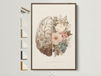 Framed floral brain artwork on a white wall. The print features a detailed brain illustration merged with delicate pastel flowers. A thin brown wooden frame surrounds the print adding a touch of warmth. Explore options like canvas or fine art paper to customize your art.