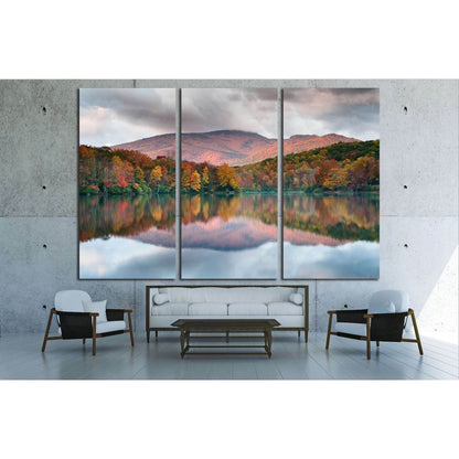 Blue Ridge Parkway Autumnal Mountain View Canvas Art for Modern OfficesThis canvas print depicts a peaceful lake reflecting the fiery hues of autumn trees and the soft purple of the mountain backdrop. The mirrored colors in the water create a sense of har